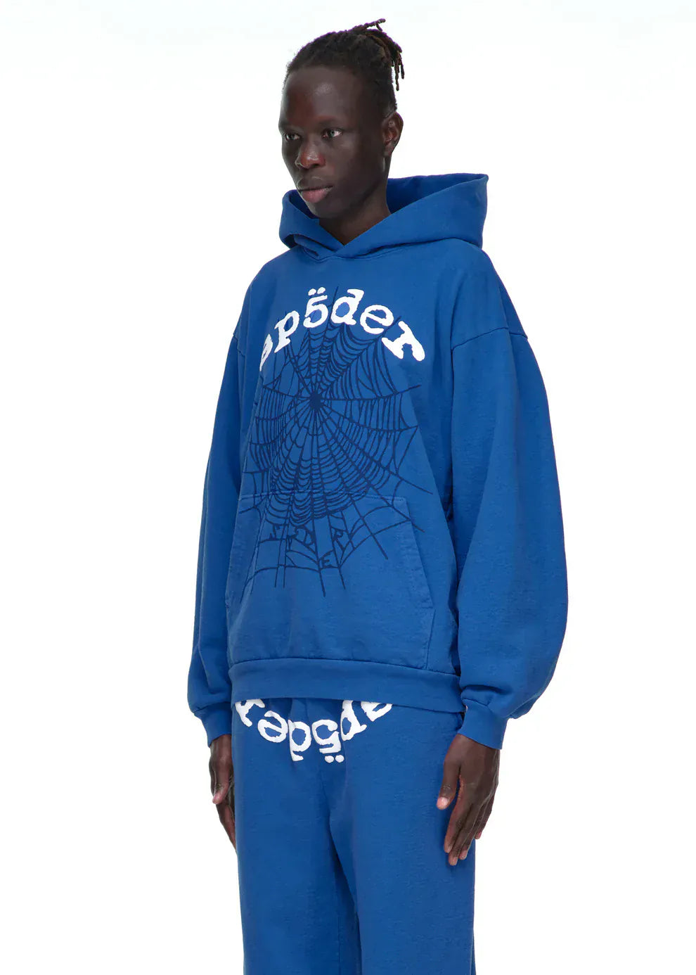A person in a royal-blue Sp5der OG Web Hoodie 440GSM Heavyweight Spider-Web Graphic Sweatshirt and matching sweatpants with SP5DER text and a spiderweb graphic stands against a white background.