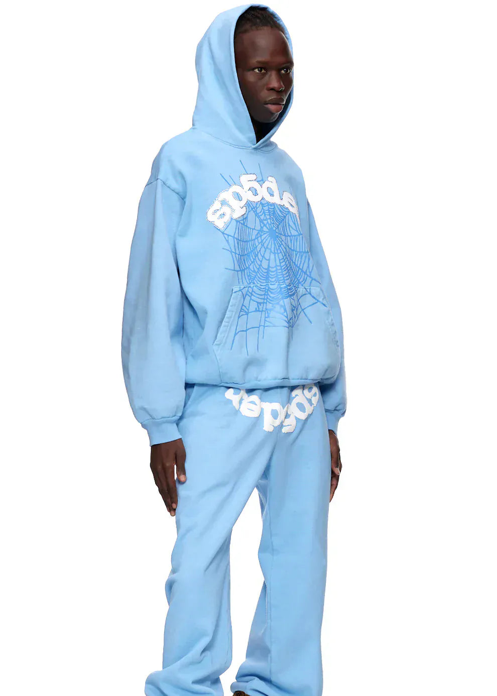 A person in a Sp5der Hoodie – Sky Blue 440GSM Heavyweight Chenille Logo Spider-Web Streetwear Pullover and matching sweatpants stands against a plain background, showcasing stylish, premium cotton fleece streetwear.