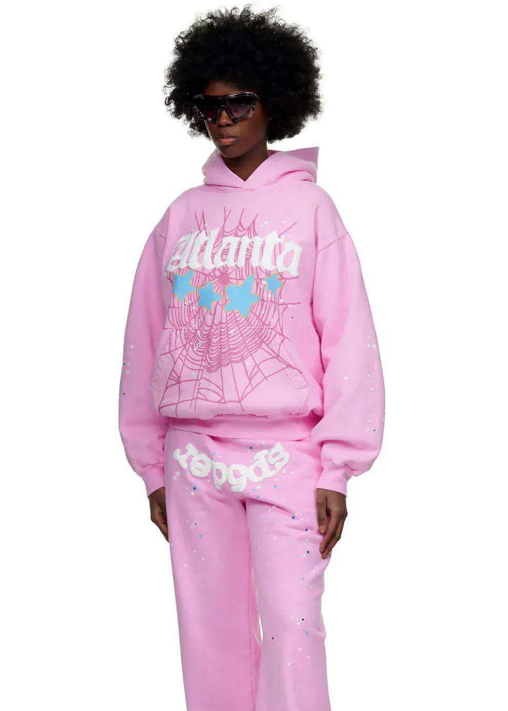 Wearing the Sp5der Atlanta Hoodie – Pink 440GSM Heavyweight Y2K Streetwear Pullover with matching pink sweatpants featuring white graphic text and web designs, this person poses against a white background in dark sunglasses.