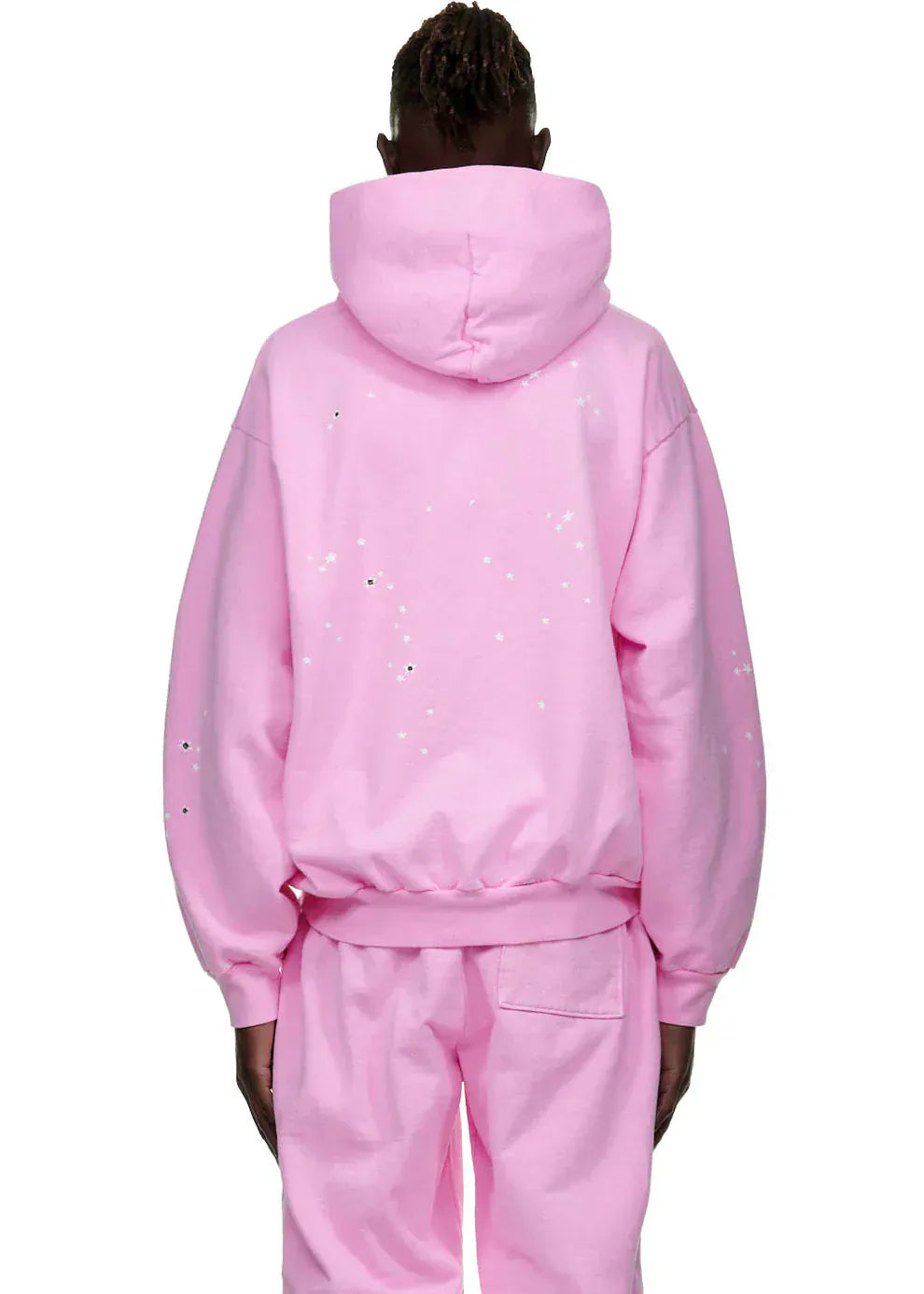 Person stands with back to camera, wearing a light pink Sp5der Atlanta Hoodie – Pink 440GSM Heavyweight Y2K Streetwear Pullover and matching pants with white specks, creating a bold Y2K streetwear vibe.