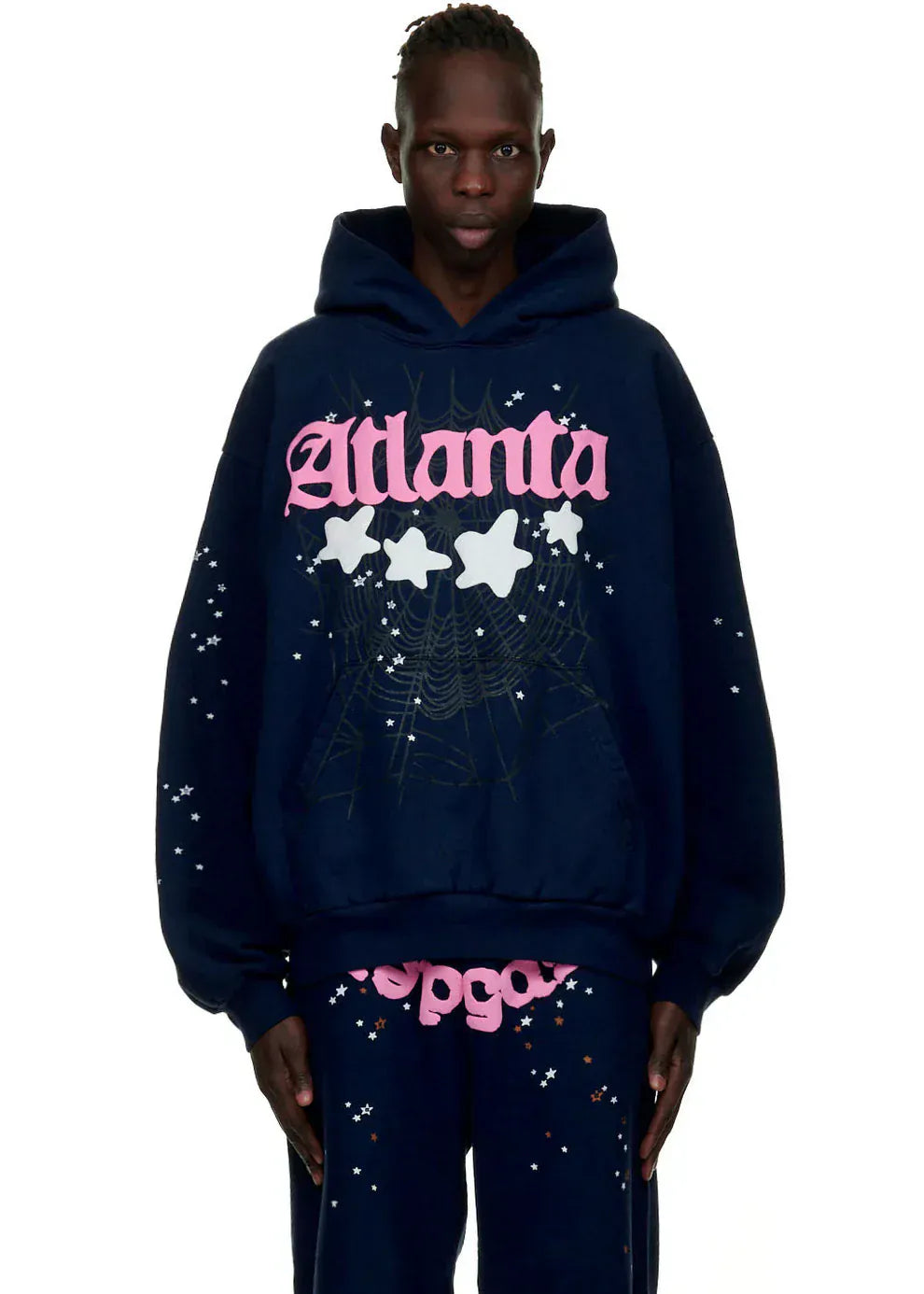 A person wears the Sp5der “Atlanta Nights” Web Hoodie in navy blue, a 440GSM heavyweight oversized streetwear pullover with pink "Atlanta" text, white stars, and a spiderweb design—ideal paired with matching pants.