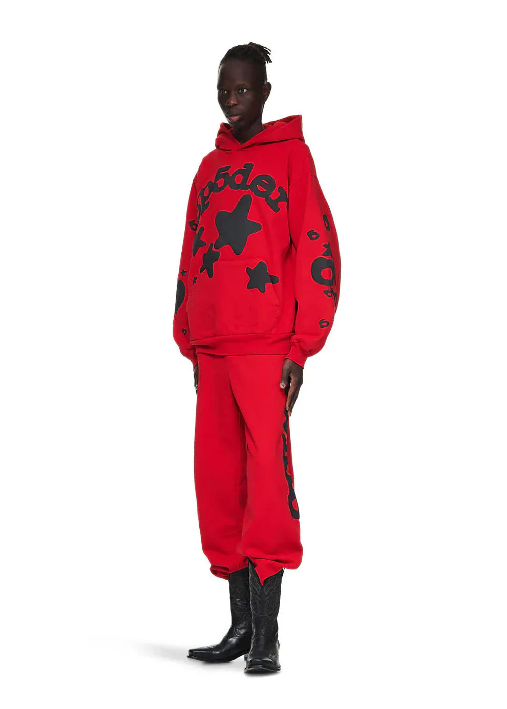 A person stands against a plain white background wearing a Sp5der “Starfire” Hoodie in red & black, a heavyweight 440GSM oversized streetwear pullover with black star designs and text, paired with matching sweatpants and black boots.