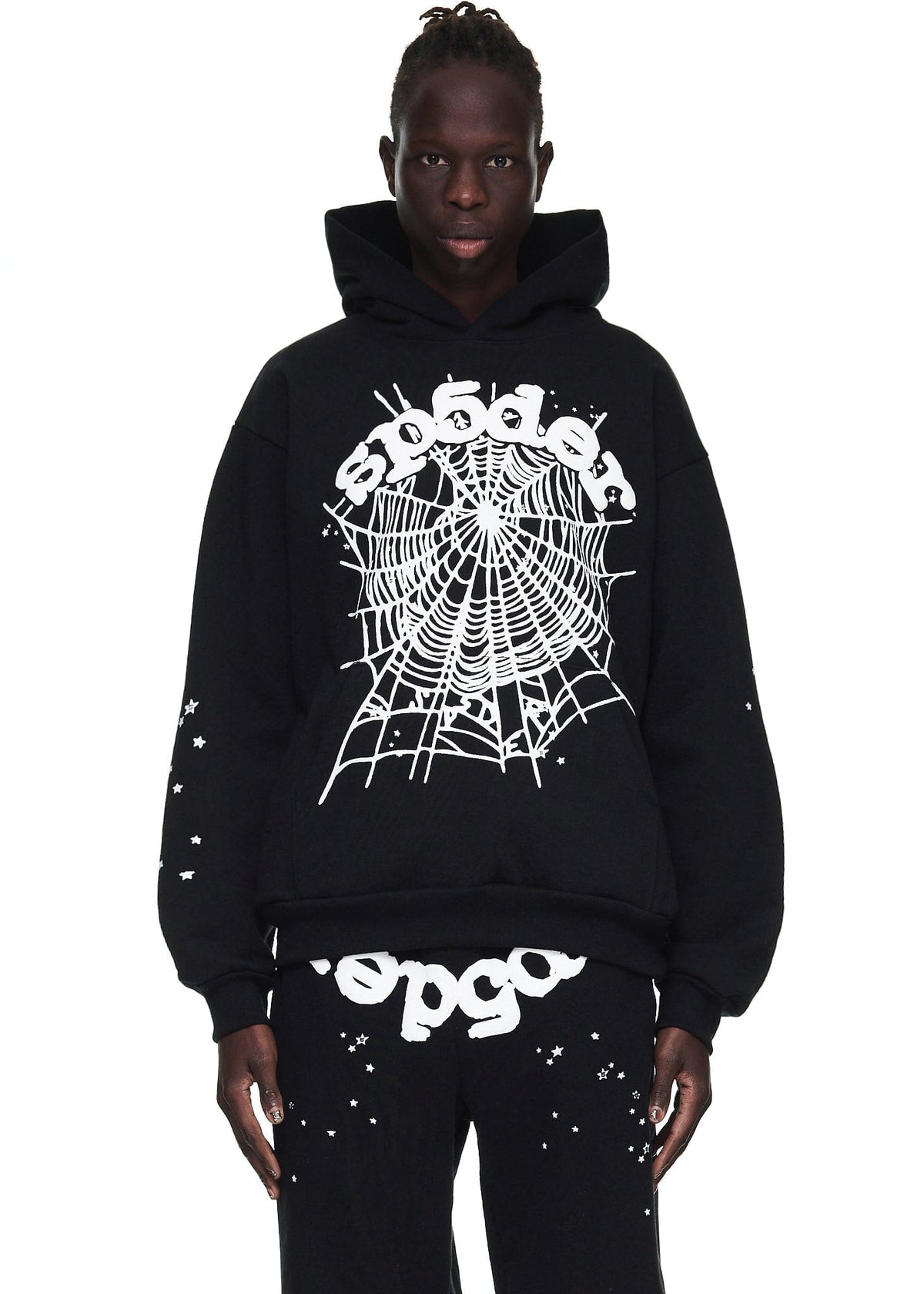 A person wears a Sp5der “Webcore Noir” Hoodie – Black & White 440GSM Heavyweight Oversized Streetwear Pullover and matching pants with white spiderweb graphics and text, standing against a white background to showcase the edgy style.