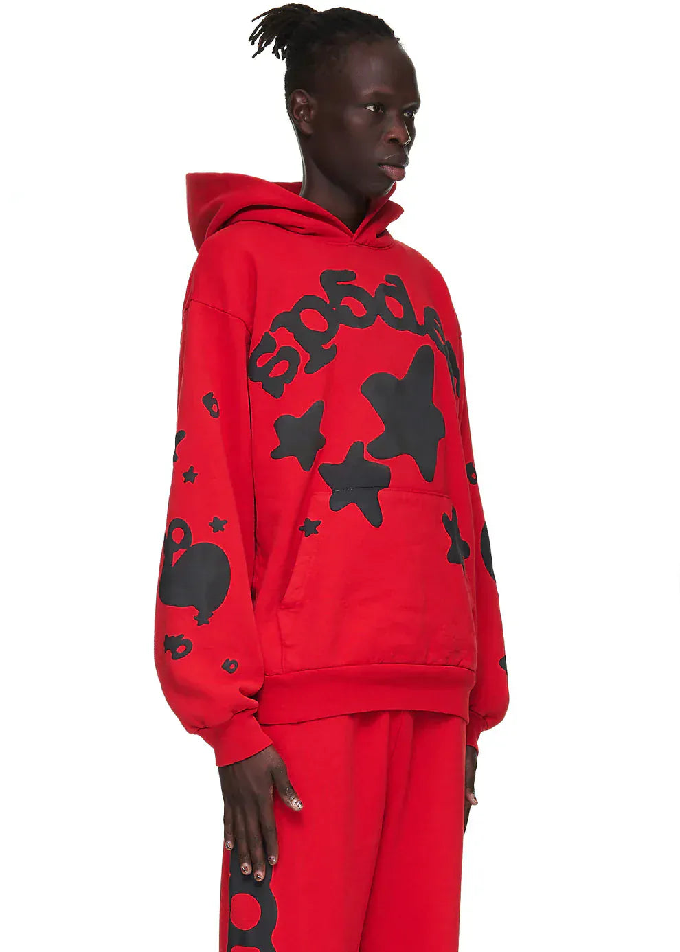 A person wears the Sp5der “Starfire” Hoodie – Red & Black 440GSM Heavyweight Oversized Streetwear Pullover with bold black graphic stars, styled with matching pants, standing against a plain white background.