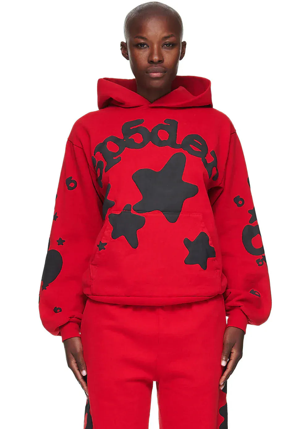 A person in the Sp5der “Starfire” Hoodie – Red & Black 440GSM Heavyweight Oversized Streetwear Pullover and matching pants, featuring large black stars and bold text—a striking streetwear statement.