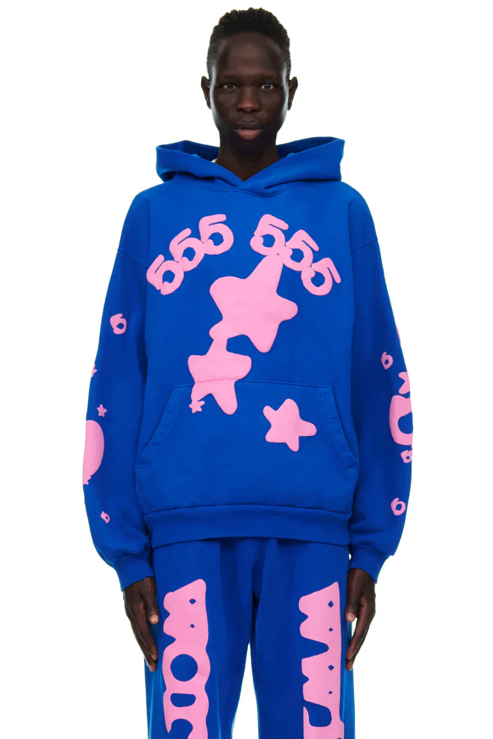 Someone in the Sp5der “555 Stars” Royal Blue/Pink Hoodie, a 440GSM heavyweight oversized streetwear pullover, paired with matching pants featuring bold pink graphics, showcases true Y2K style.