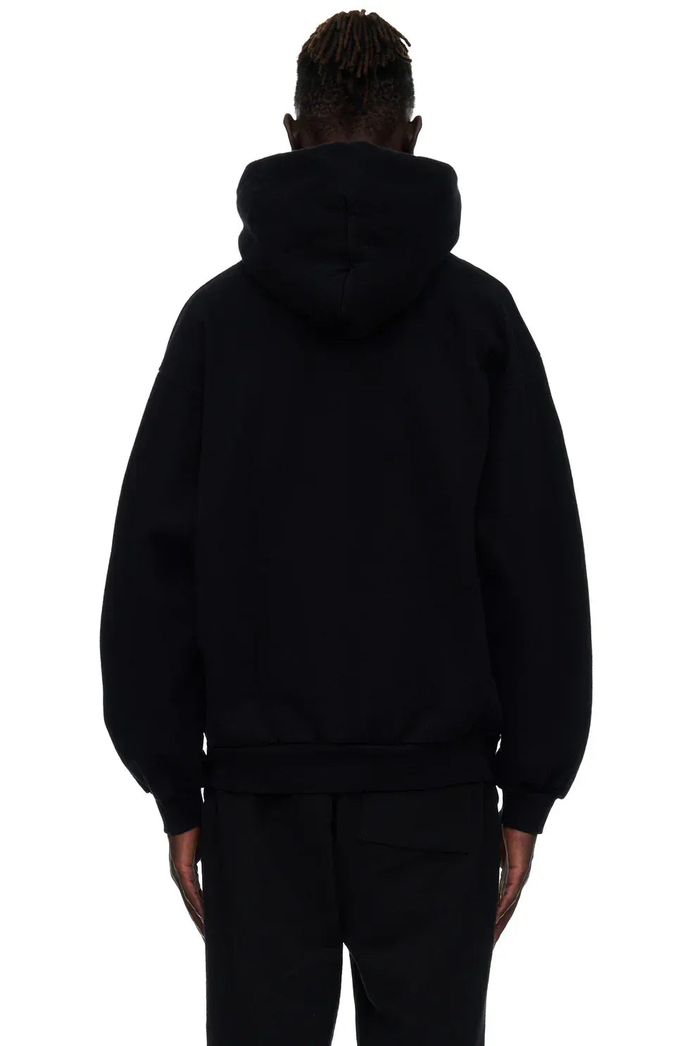 A person is shown from the back in a minimalist streetwear style, wearing a black Sp5der “I Love Sp5der” Hoodie – Black Web 440GSM Heavyweight Pullover and black pants against a plain white background.
