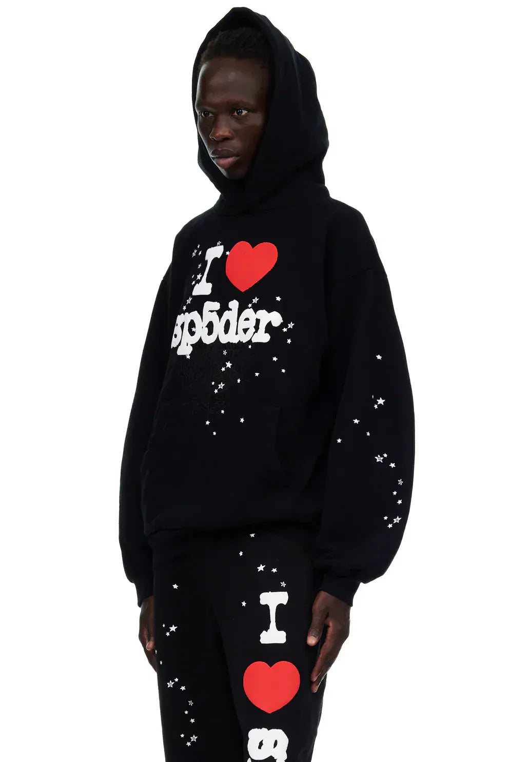 Model wearing the Sp5der “I Love Sp5der” Hoodie – Black Web 440GSM heavyweight pullover with white "I ♥ sp5der" text and star patterns, embodying a Y2K streetwear style against a white backdrop.