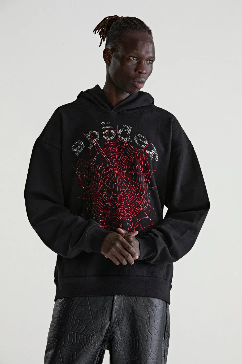 Model wears a Sp5der Rhinestone Web Hoodie – Black 440GSM Heavyweight Oversized Streetwear Pullover with red web and silver text, paired with matching black web-patterned pants, standing against a plain background.