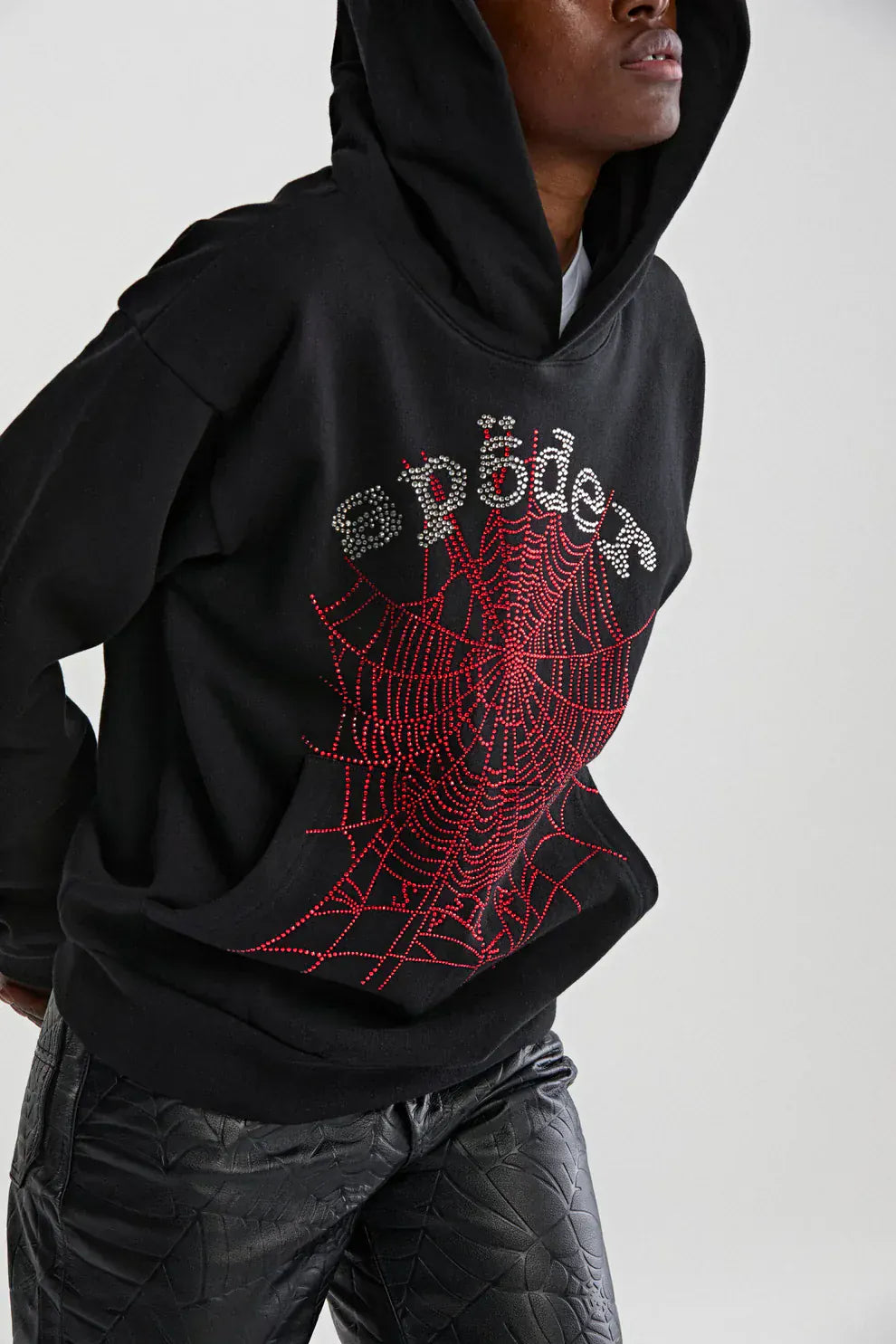 Wearing a Sp5der Rhinestone Web Hoodie – Black 440GSM Heavyweight Oversized Streetwear Pullover with rhinestone web and text design, paired with black pants for a luxury streetwear vibe.