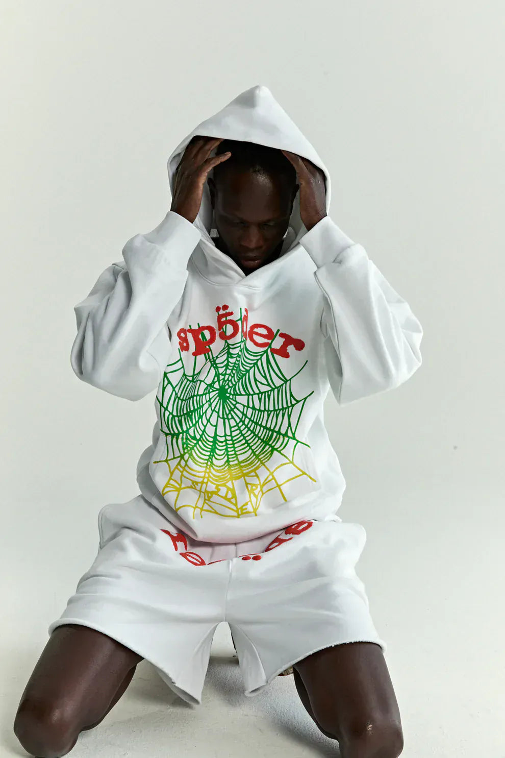 Wearing the Sp5der “Toxic Web” Hoodie – White & Neon Lime 440GSM Heavyweight Oversized Streetwear Pullover, a person sits on the floor adjusting their hood, channeling Y2K streetwear vibes with bold neon web graphics.