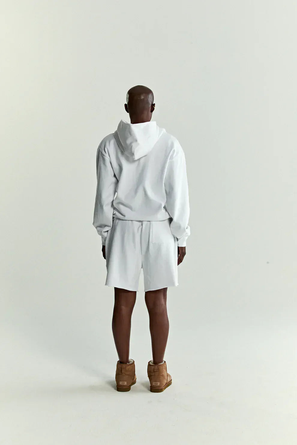 A person with a shaved head, wearing the Sp5der “Toxic Web” Hoodie in white & neon lime (440GSM heavyweight oversized pullover) and white shorts, stands facing away from the camera against a plain white background in Y2K streetwear style.