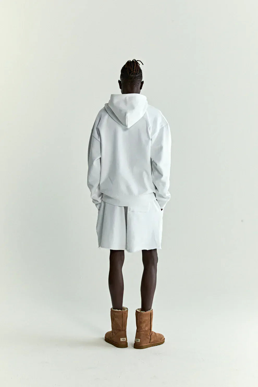 A person stands facing away, wearing a Sp5der “Toxic Web” Hoodie – White & Neon Lime 440GSM Heavyweight Oversized Streetwear Pullover, paired with white shorts and brown boots against a plain light background.
