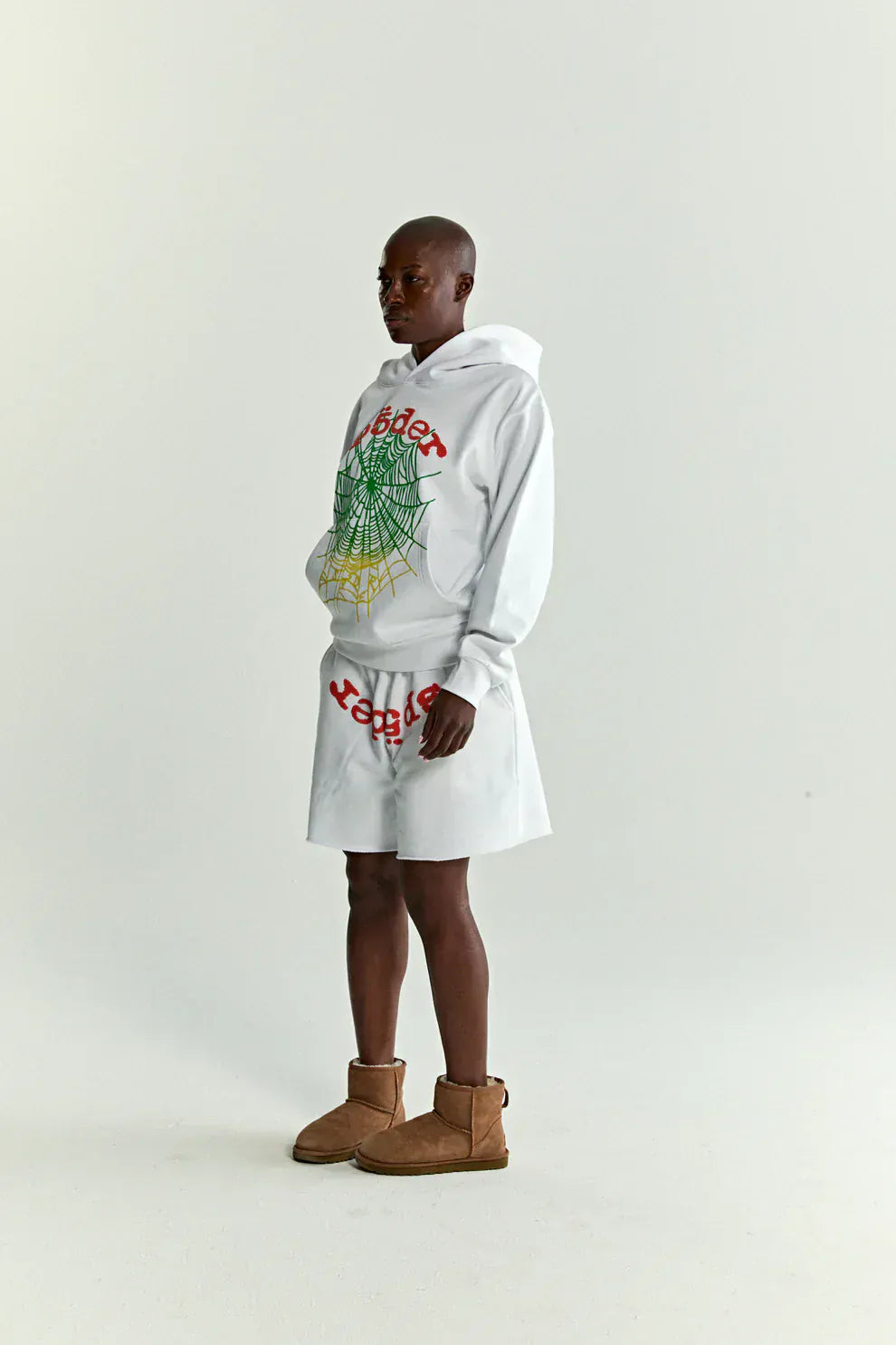 Person in profile wears a Sp5der “Toxic Web” Hoodie – White & Neon Lime 440GSM Heavyweight Oversized Streetwear Pullover, white shorts, and brown ankle boots—exuding Y2K streetwear style against a plain light background.