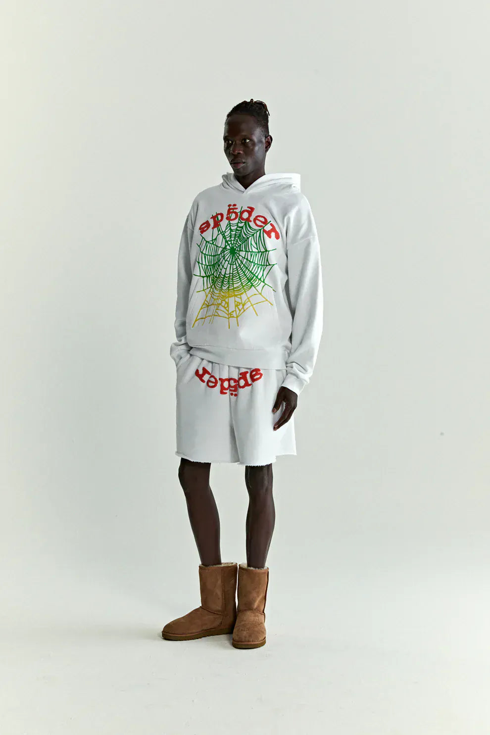 A person wears the Sp5der “Toxic Web” Hoodie in White & Neon Lime (440GSM heavyweight, oversized pullover) with matching shorts and brown boots, standing against a plain backdrop for a bold Y2K streetwear vibe.