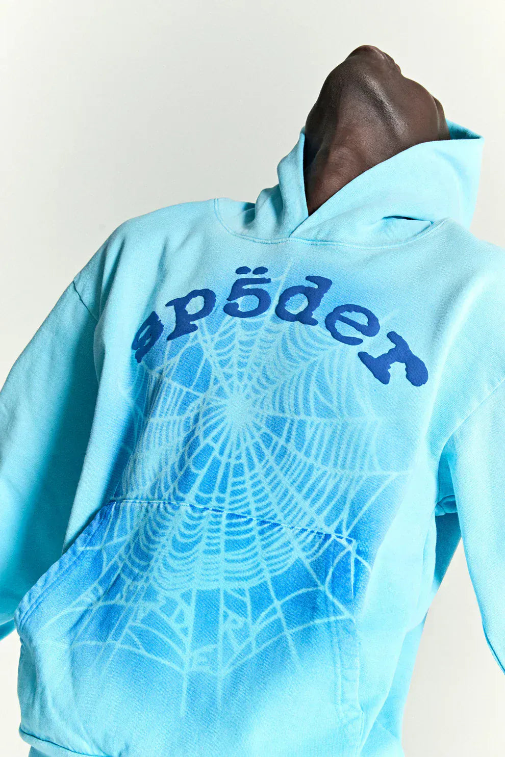 Model wears the Sp5der “Blue Venom” Web Hoodie – Sky Blue Fade, a 440GSM heavyweight oversized streetwear pullover with spiderweb graphics and blue “spöder” text, leaning back with head tilted for a bold look.