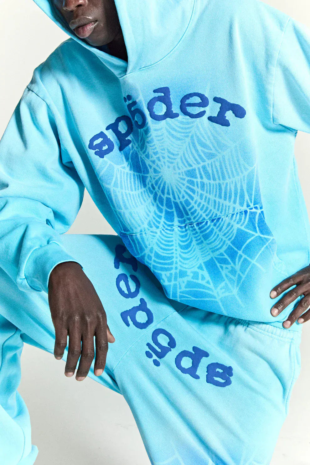 A person wears the Sp5der “Blue Venom” Web Hoodie – Sky Blue Fade 440GSM heavyweight oversized streetwear pullover, flaunting bold “sp5der” text and a striking blue spiderweb graphic for authentic streetwear vibes.