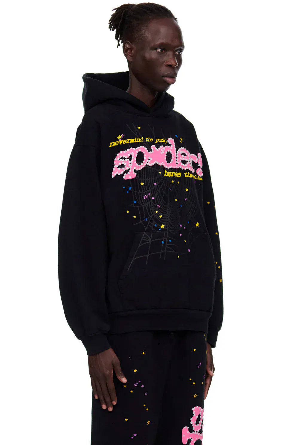 A person wears the Sp5der “Hares the Slime” Hoodie—Black 440GSM heavyweight streetwear pullover with colorful spider text, a spider web graphic, and matching black pants with stars and pink lettering.