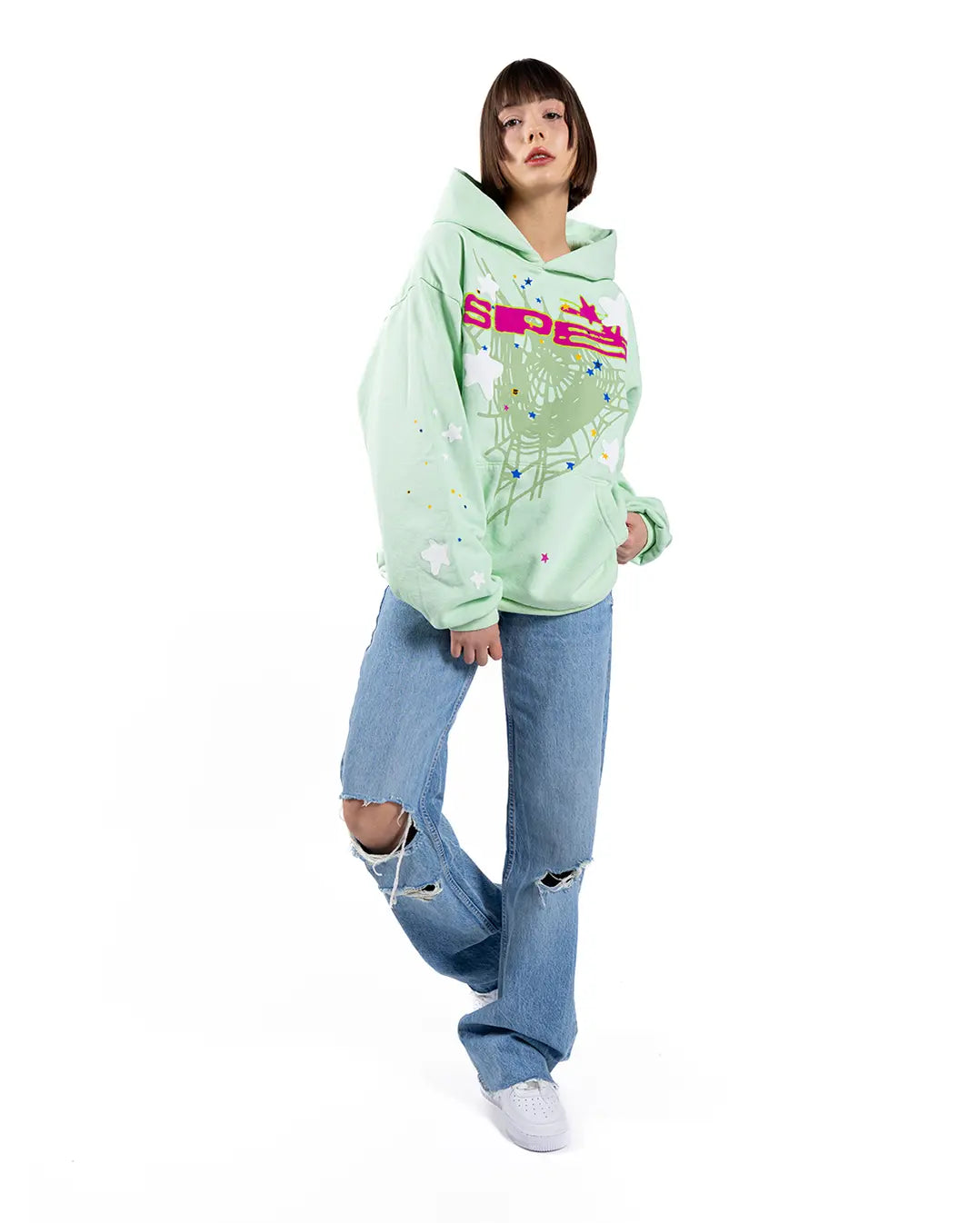 A person wears the Sp5der “Mint Star Web” Hoodie in mint green—an oversized 440GSM heavyweight streetwear pullover—paired with ripped blue jeans and white sneakers, capturing Y2K streetwear style against a plain white background.