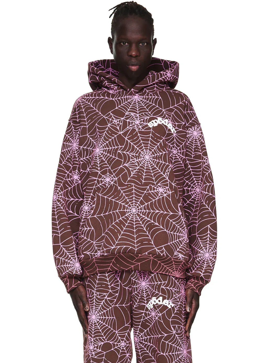 A person wears the Brown All-Over Spider Web Graphic Hoodie, a comfort-fit pullover in brown with an all-over light pink spider web print and a small white chest logo.