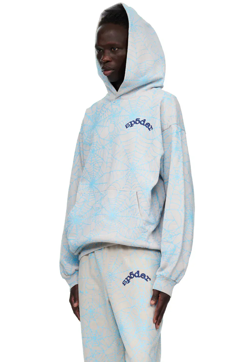 A person wearing a light grey comfort fit pullover hoodie with an all-over spider web graphic, featuring the sp5der logo.