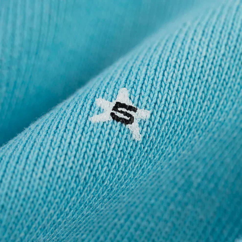 Close-up of the Turquoise Graphic Hoodie’s soft knit fabric, showing a white star and bold black "S" embroidery—part of this comfort-fit pullover with spider web back print.