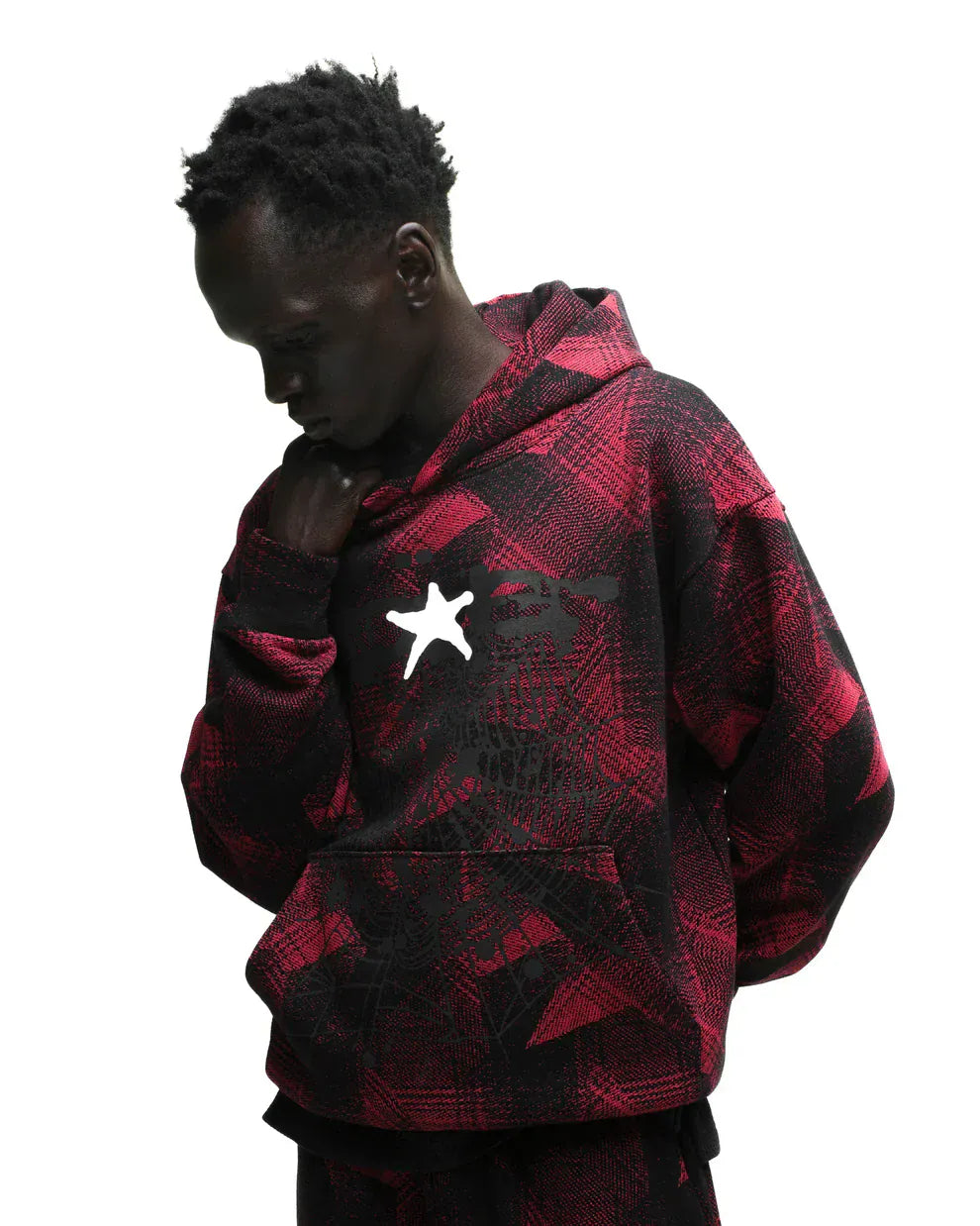 A person models the Red and Black Graphic Hoodie with Star Detail and Spider Web Print – Comfort Fit Pullover, standing against a white background in streetwear style, looking down with one hand near their face.