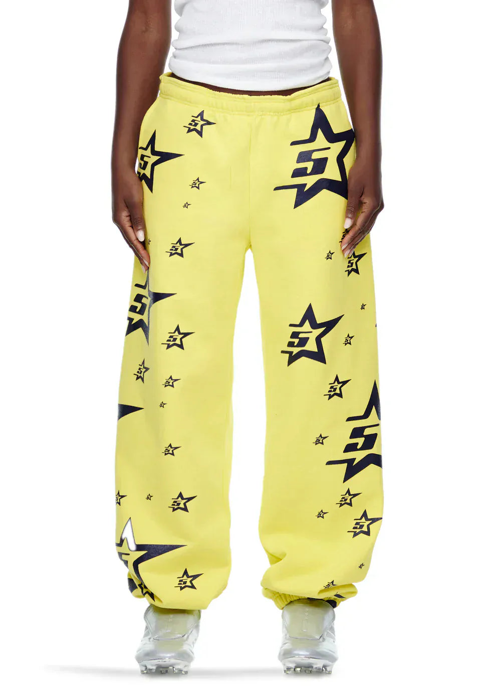 Someone in Sp5der Sweatpants—Unisex Yellow Cotton Sweatpants with All-Over Star Print—and a white tank top stands against a plain background, creating an effortless streetwear vibe.