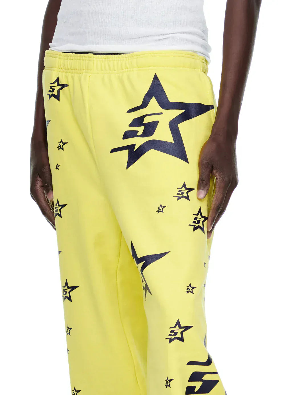 Person wearing Sp5der Sweatpants – Unisex Yellow Cotton Sweatpants with All-Over Star Print and a white ribbed tank top, serving standout streetwear vibes.