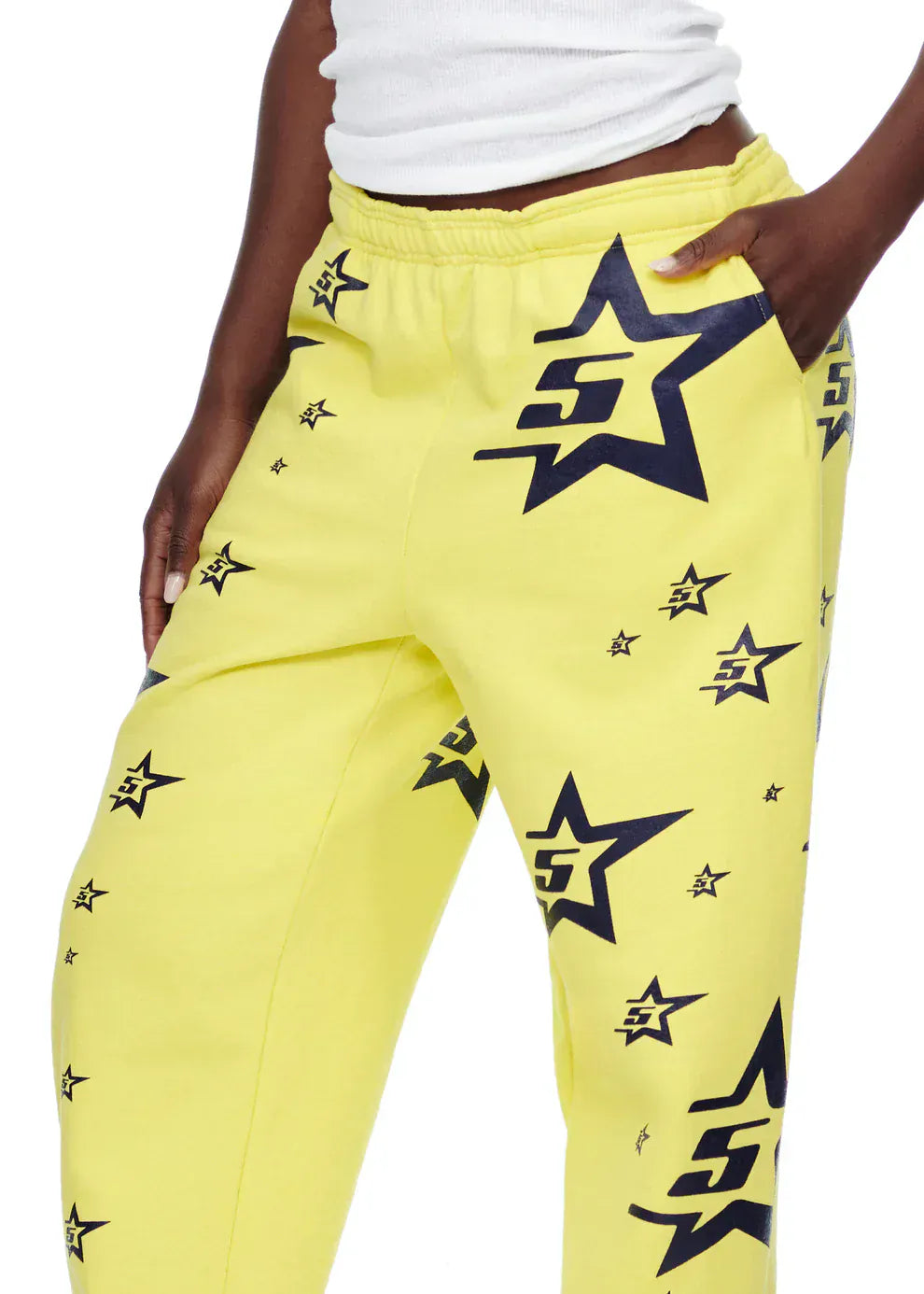 A person wears Sp5der Sweatpants – unisex yellow cotton sweatpants with an all-over star print – paired with a white ribbed tank top, highlighting bold streetwear style.