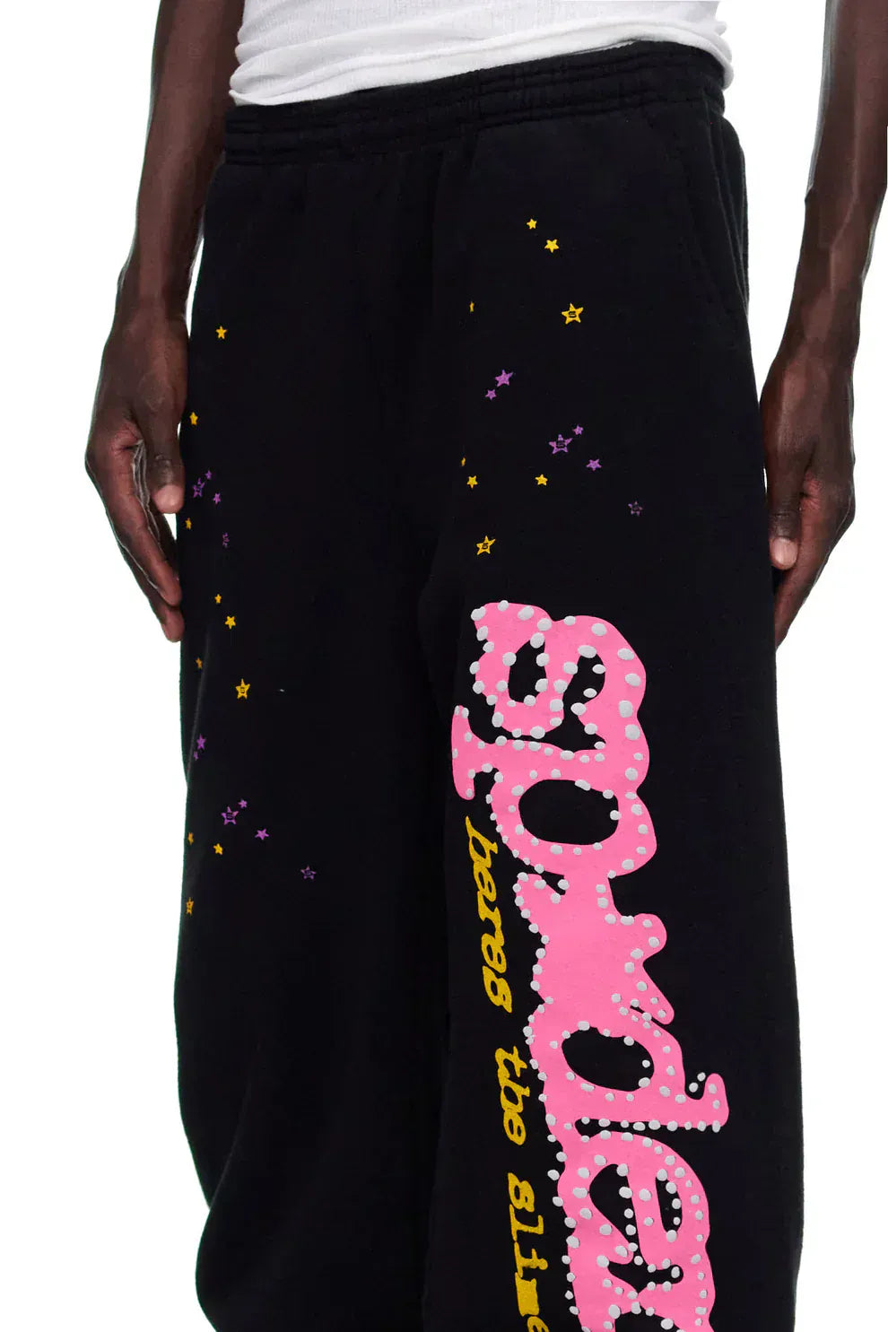 Person wearing Sp5der Sweatpants – unisex black cotton sweatpants with a pink graphic logo and star print, showcasing a streetwear vibe.