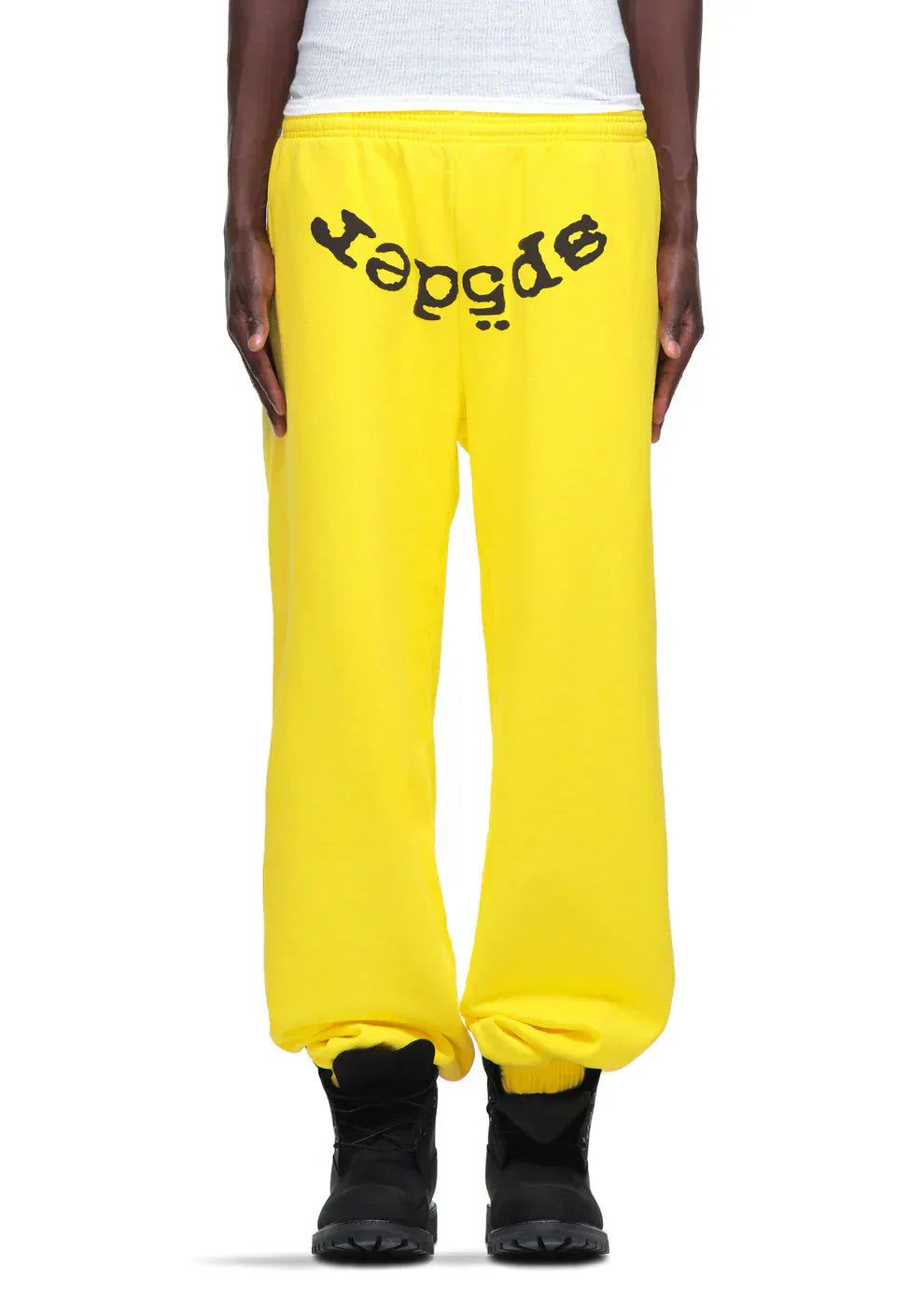 Someone styled the Sp5der Sweatpants – Unisex Yellow Cotton Sweatpants with front logo print, pairing them with black boots and a white top for a bold streetwear joggers look.