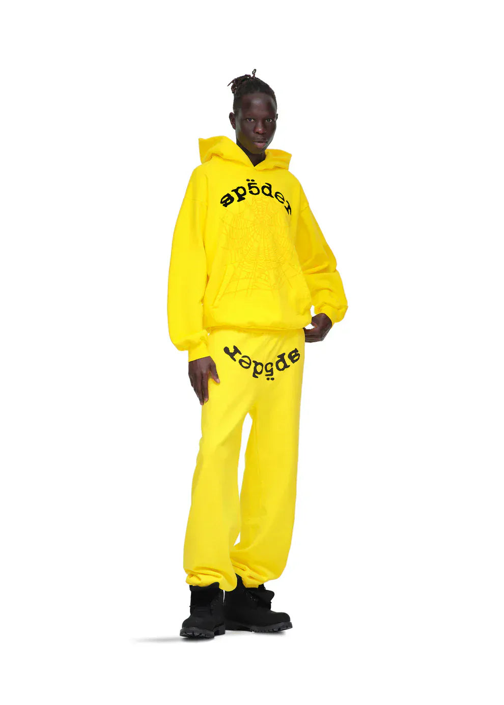 A person wears Sp5der Sweatpants – Unisex Yellow Cotton Sweatpants with front logo print, adding a bold streetwear joggers vibe against a crisp white background.