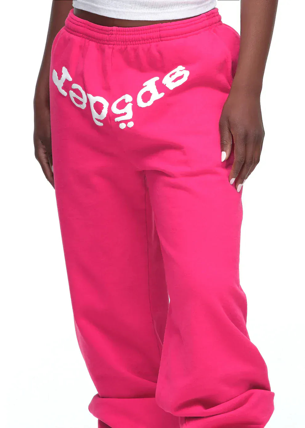 Wearing Sp5der Sweatpants – unisex pink cotton sweatpants with a white upside-down "speed" logo on the front—styled with a white ribbed tank top for standout pink streetwear flair.