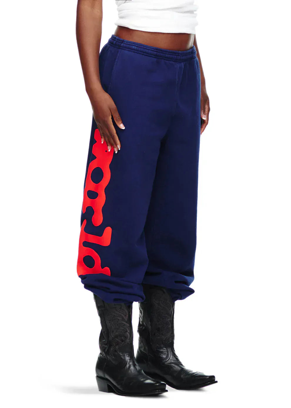A person wearing Sp5der Sweatpants Navy Blue Red Side Logo Print 100% Cotton Streetwear Jogger Pants, paired with a white top and black cowboy boots.
