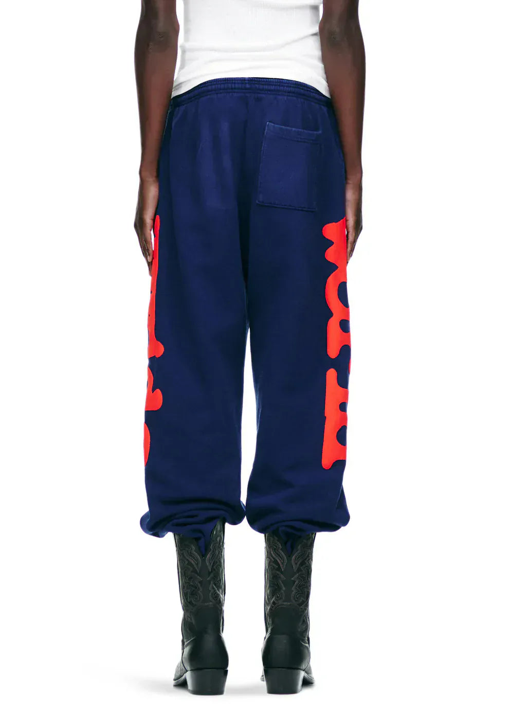 Person wearing Sp5der Sweatpants Navy Blue Red Side Logo Print – 100% Cotton Streetwear Jogger Pants, paired with black boots and a white top, shown from the back.