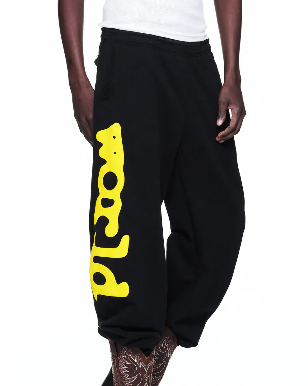 A person rocks Sp5der Sweatpants Black Yellow Side Logo Print – 100% Cotton Streetwear Jogger Pants with a white top and tattooed legs, nailing the ultimate streetwear joggers style.