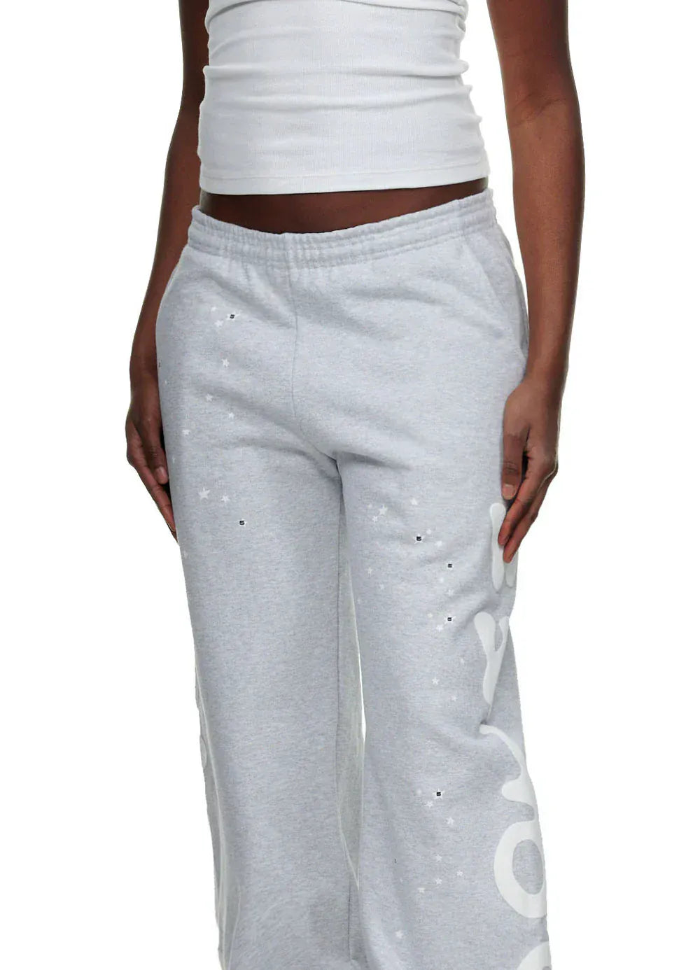 A person is wearing a white sleeveless top and 100% Cotton Sp5der Sweatpants for Men – Grey Streetwear Jogger Pants with graphic print and relaxed fit, standing with arms relaxed at their sides.