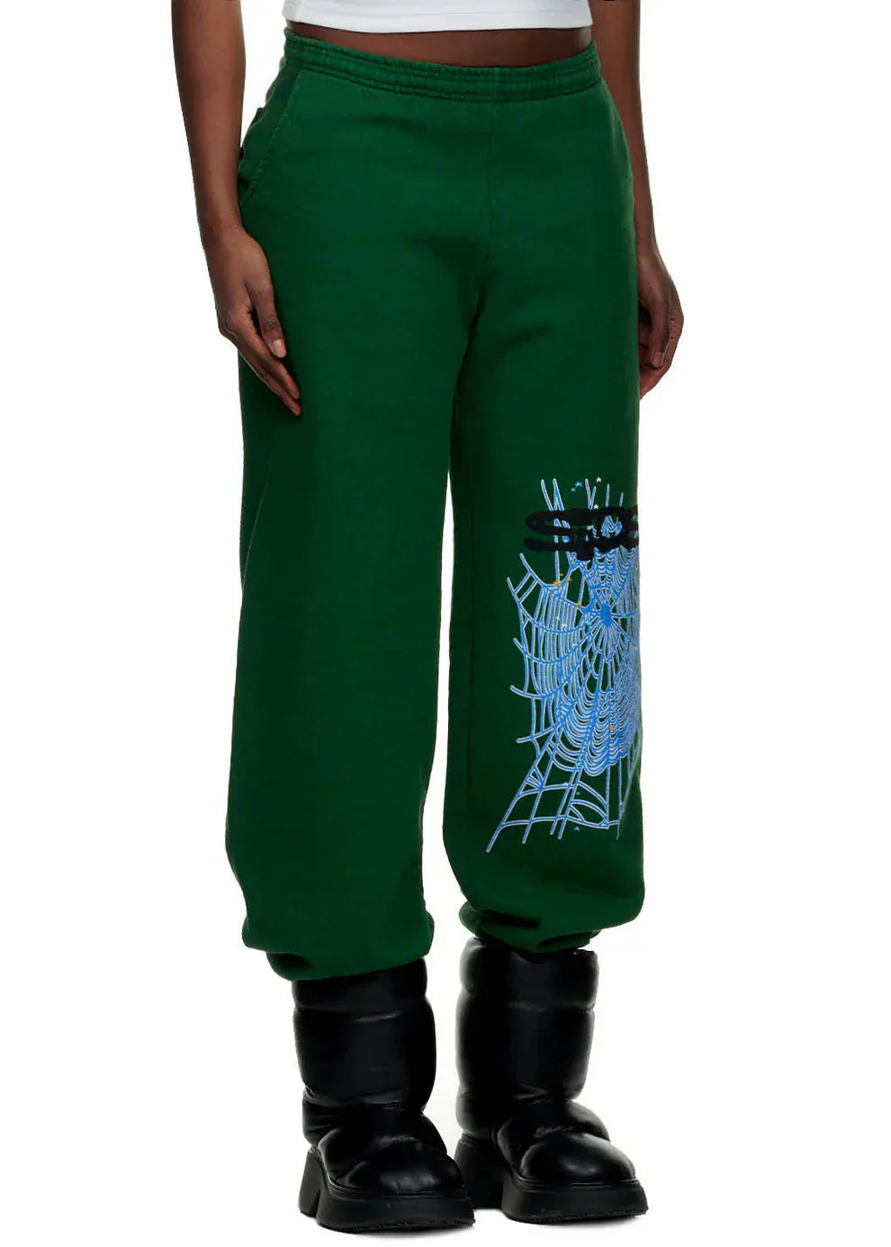 A person wearing 100% Cotton Sp5der Sweatpants for Men – Dark Green Streetwear Jogger Pants with Spider Web Graphic, styled with black boots, shown from torso to feet.