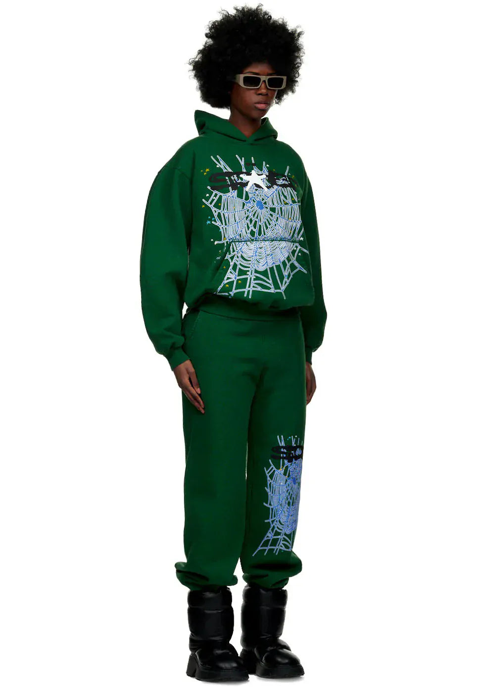 Person wears a green hoodie, 100% Cotton Sp5der Sweatpants for Men – Dark Green Streetwear Jogger Pants with Spider Web Graphic (Relaxed Fit), black boots, and sunglasses, standing against a plain background.