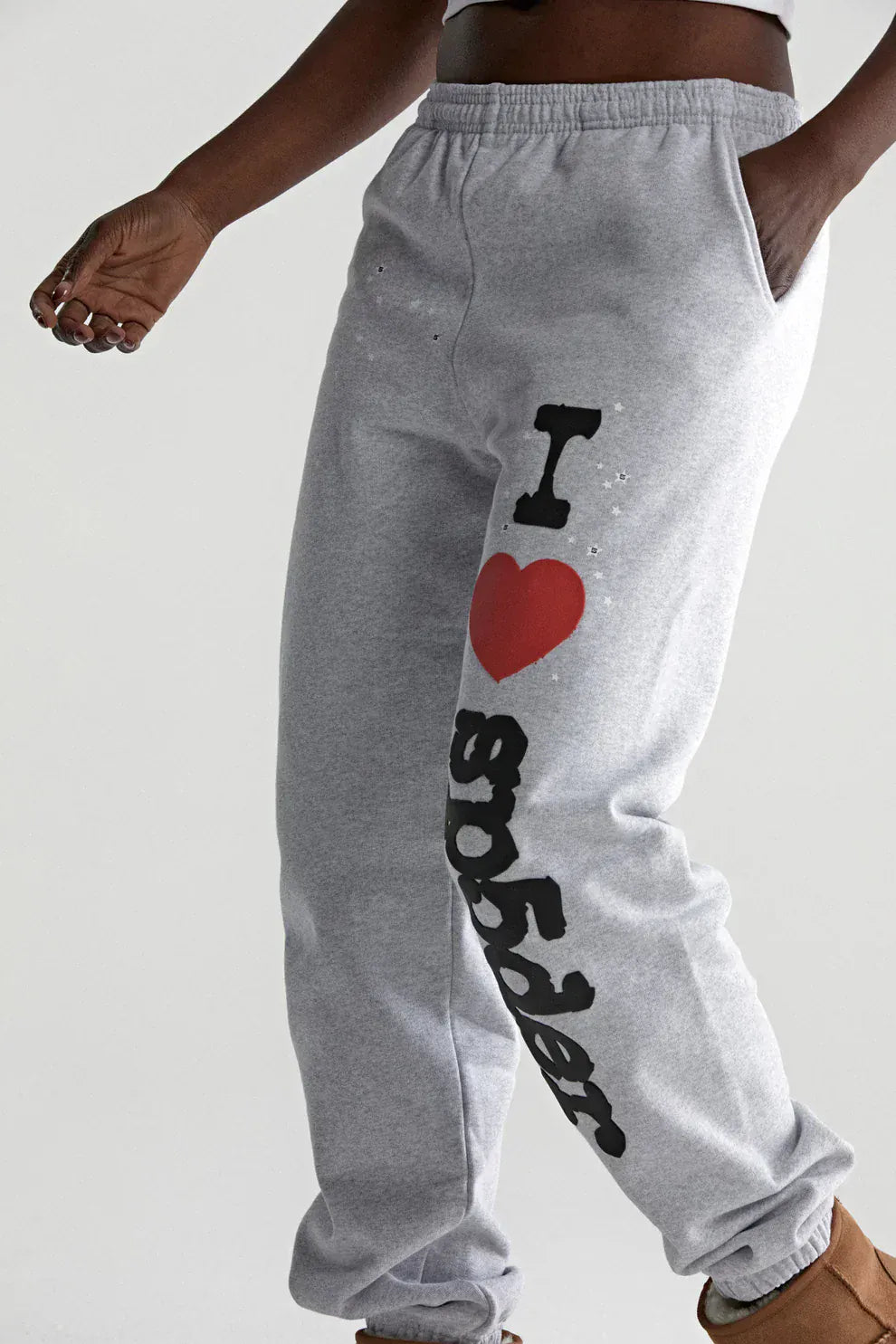 A person wearing light grey 100% cotton Sp5der sweatpants with a bold “I Love Sp5der” graphic down the leg and one hand in the pocket—a playful update to classic relaxed fit joggers.
