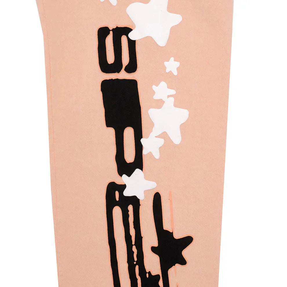 A peach section of 100% cotton Sp5der Sweatpants—unisex jogger pants with a vertical logo and white star graphics—shows black abstract shapes printed on soft, relaxed-fit material.