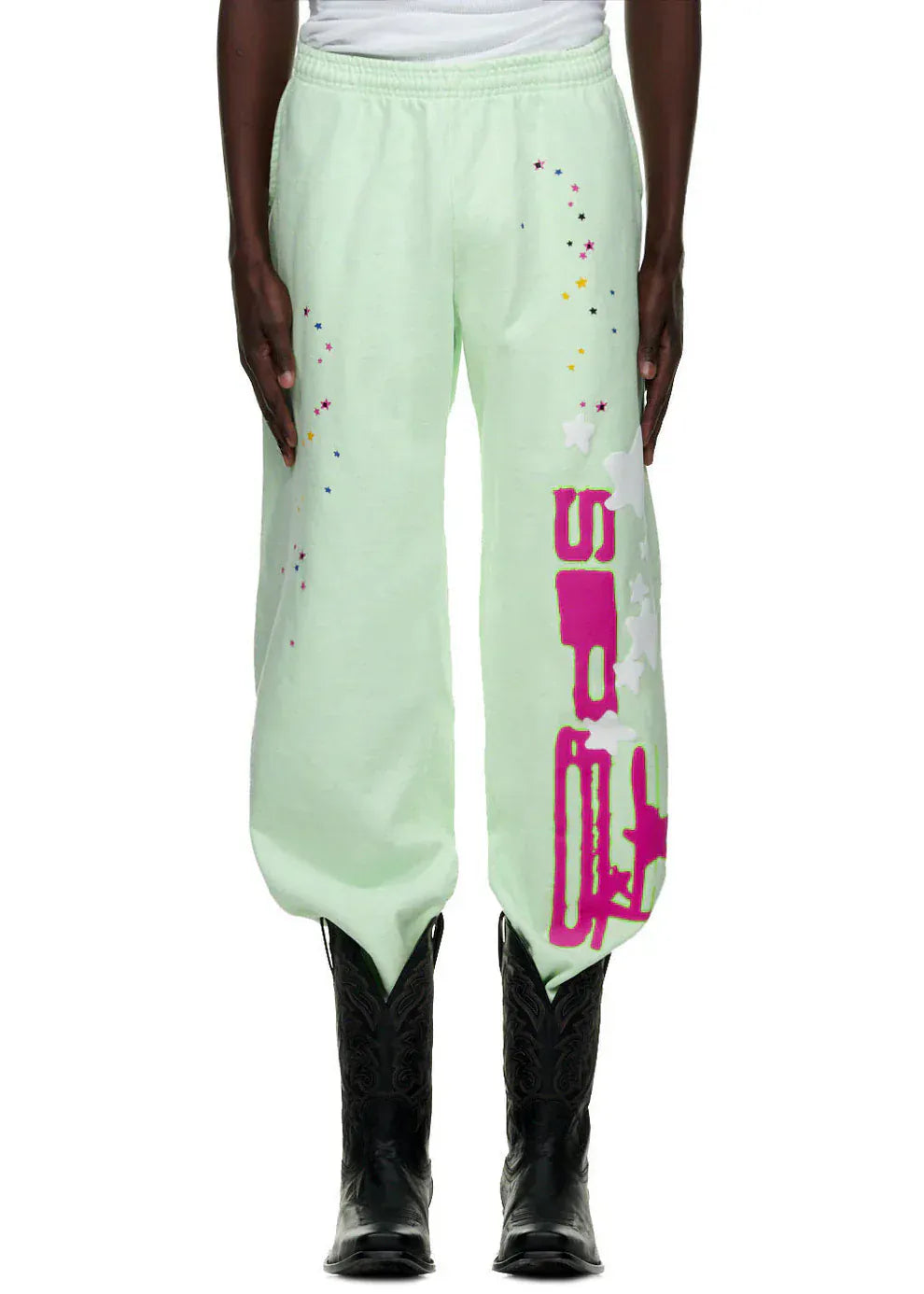Person wearing 100% Cotton Sp5der Sweatpants–Unisex Mint Green Jogger Pants with vertical logo and star graphics, relaxed fit; styled with black cowboy boots and a white top. Only the lower torso and legs are shown.