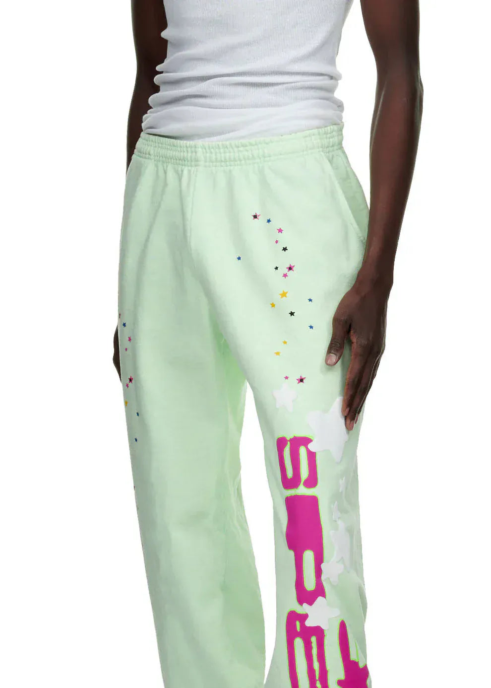 A person wears unisex 100% cotton Sp5der Sweatpants—mint green joggers with a vertical logo and star graphics, relaxed fit—paired with a white ribbed tank top. Only the torso and legs are visible.