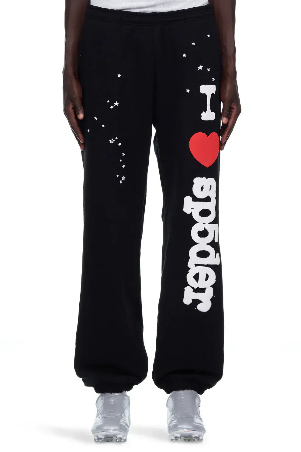 Someone wears 100% Cotton Sp5der Sweatpants—Unisex Black Jogger Pants featuring “I Love Sp5der” and white star graphics on the left leg, paired with white shoes for a relaxed, streetwear look.