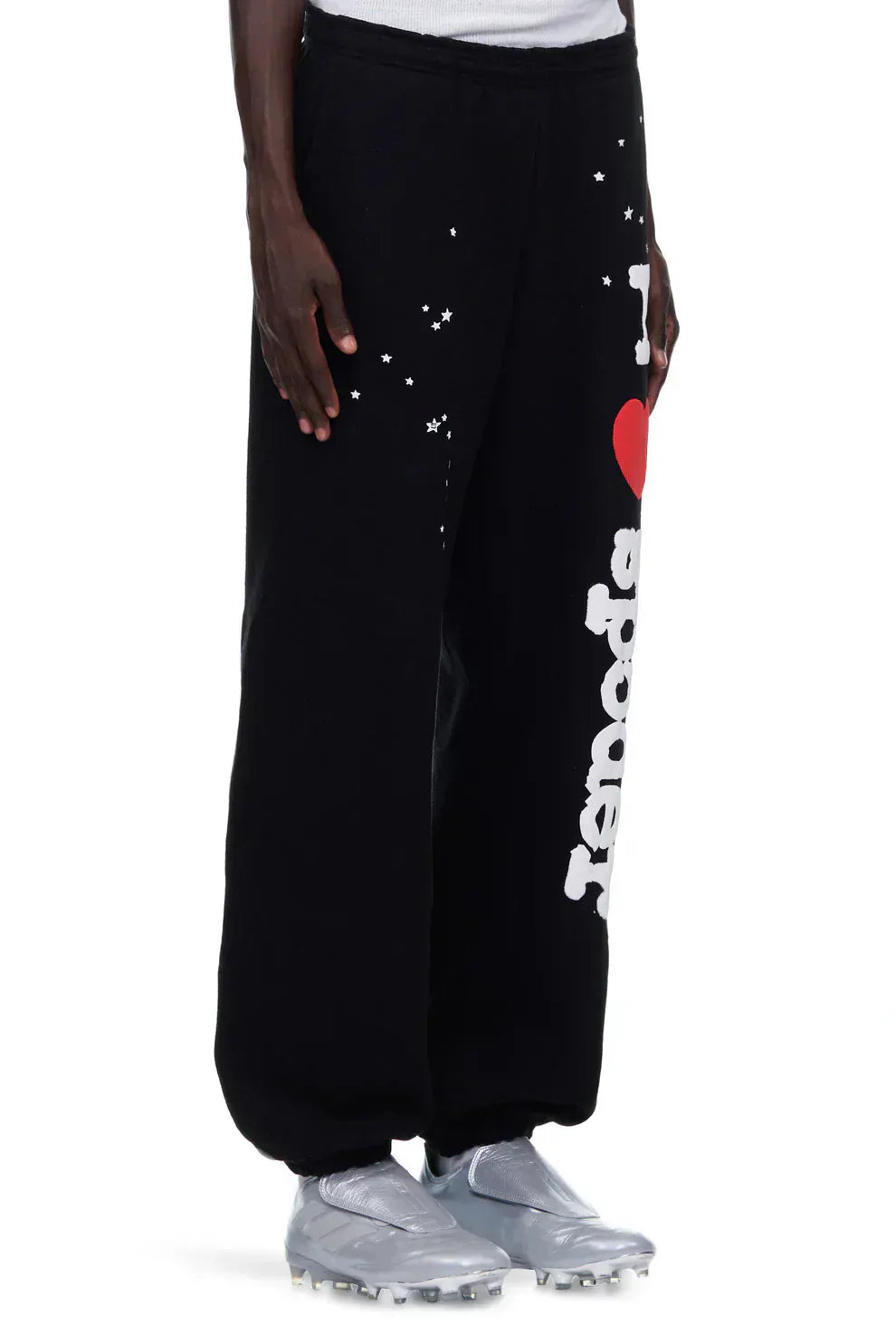 A person wearing 100% cotton Sp5der unisex black jogger pants with a relaxed fit and “I Love Sp5der” graphic, paired with silver athletic shoes.