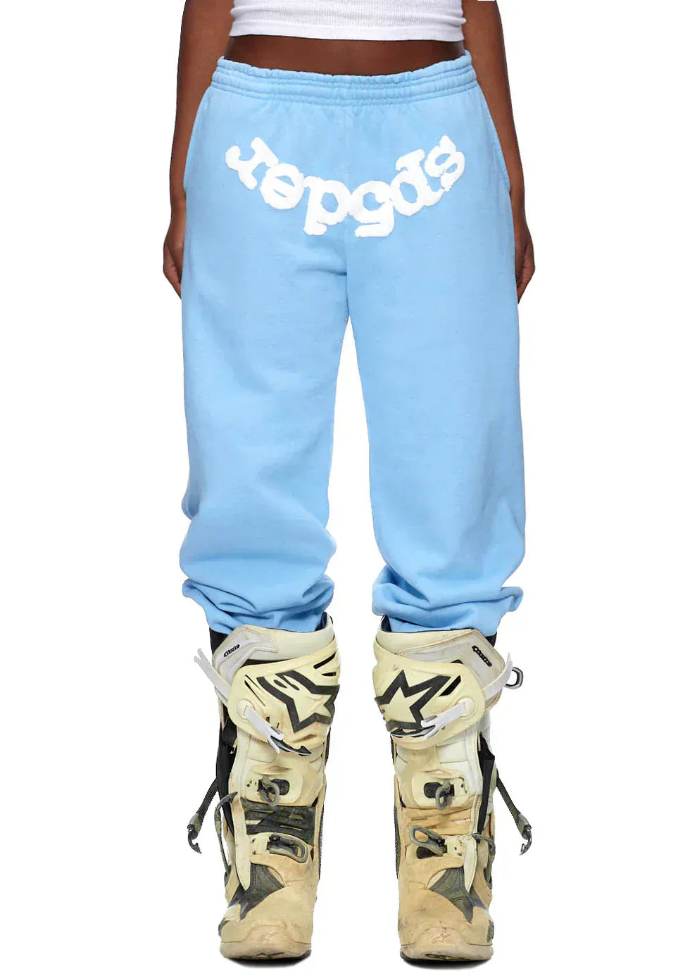 Person wearing Sp5der Sweatpants – Unisex Light Blue Cotton Sweatpants with front logo print, styled with white motocross boots, shown from waist to feet—a bold streetwear statement.