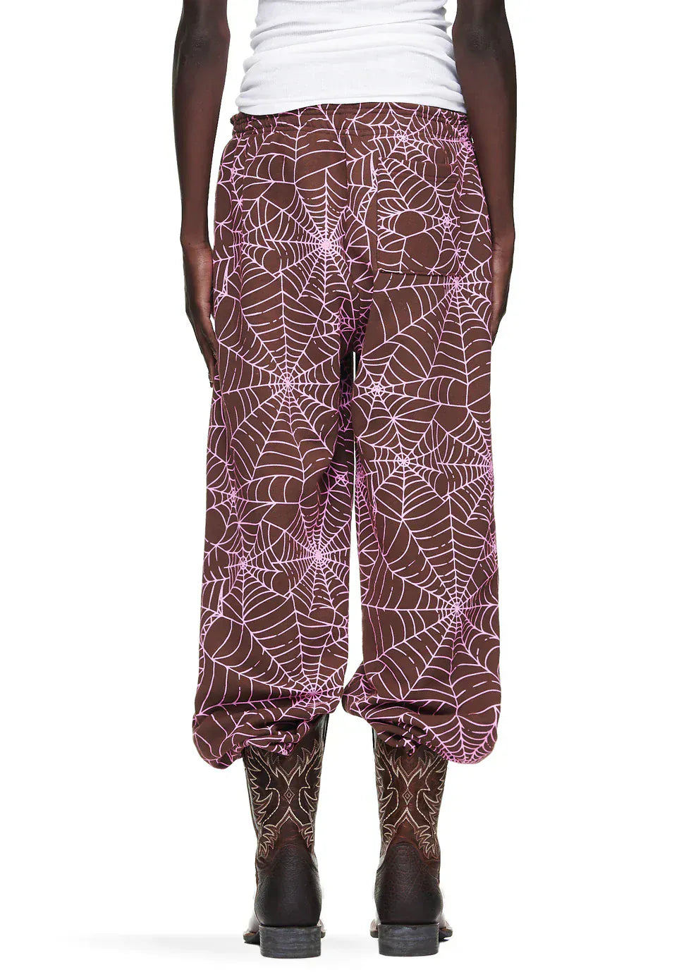 A person wears 100% Cotton Sp5der Sweatpants—Unisex Brown Jogger Pants with All-Over Spider Web Print, relaxed fit—and matching boots, shown from the back against a plain background for standout streetwear style.