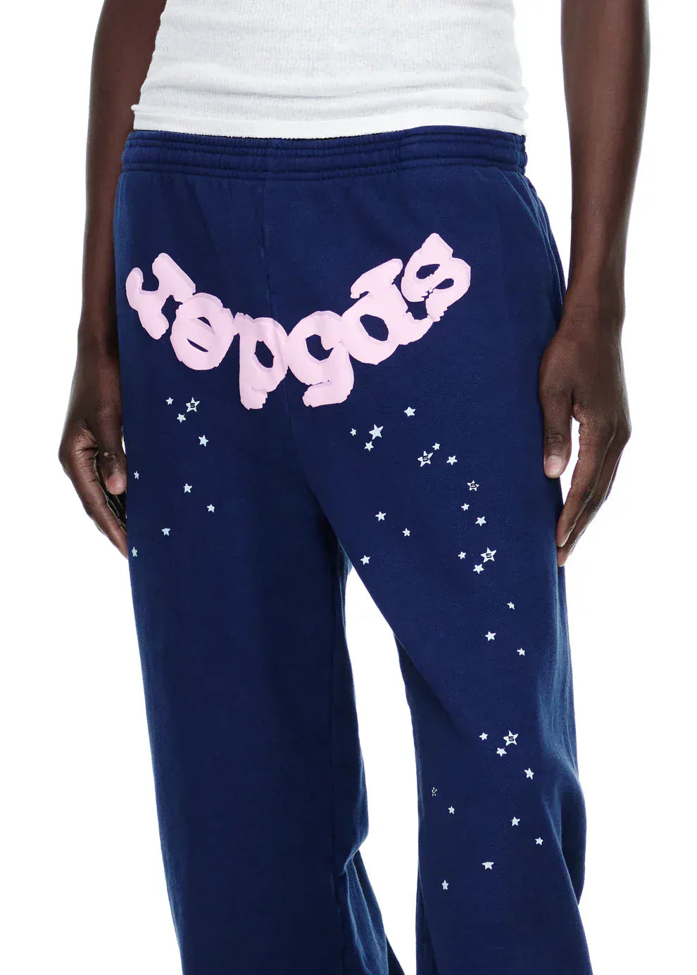 A person wears 100% Cotton Sp5der Sweatpants—unisex navy blue joggers with a pink logo and star graphics, featuring a relaxed fit.