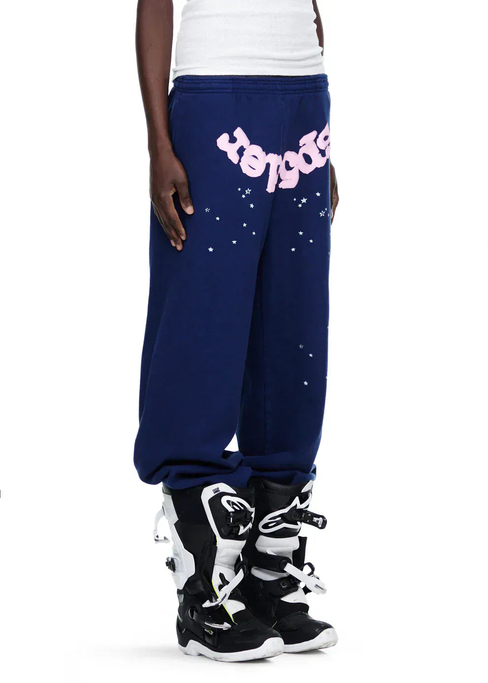 A person in 100% Cotton Sp5der Sweatpants—Unisex Navy Blue Jogger Pants with a pink logo and star graphics—pairs them with black motocross boots, standing against a plain background. Effortlessly stylish and comfortable.